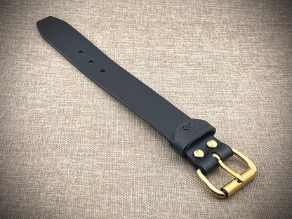 Black leather strap with brass buckle on a textured beige background