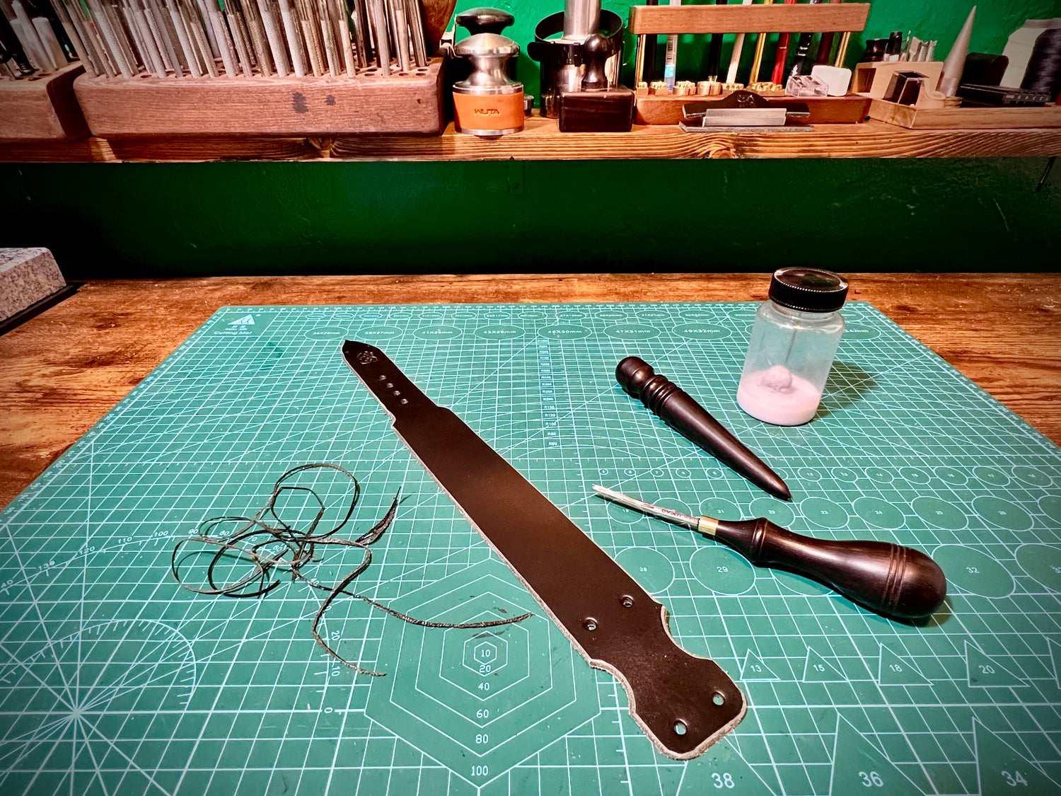 Leather working tools on a green cutting mat with a workshop background
