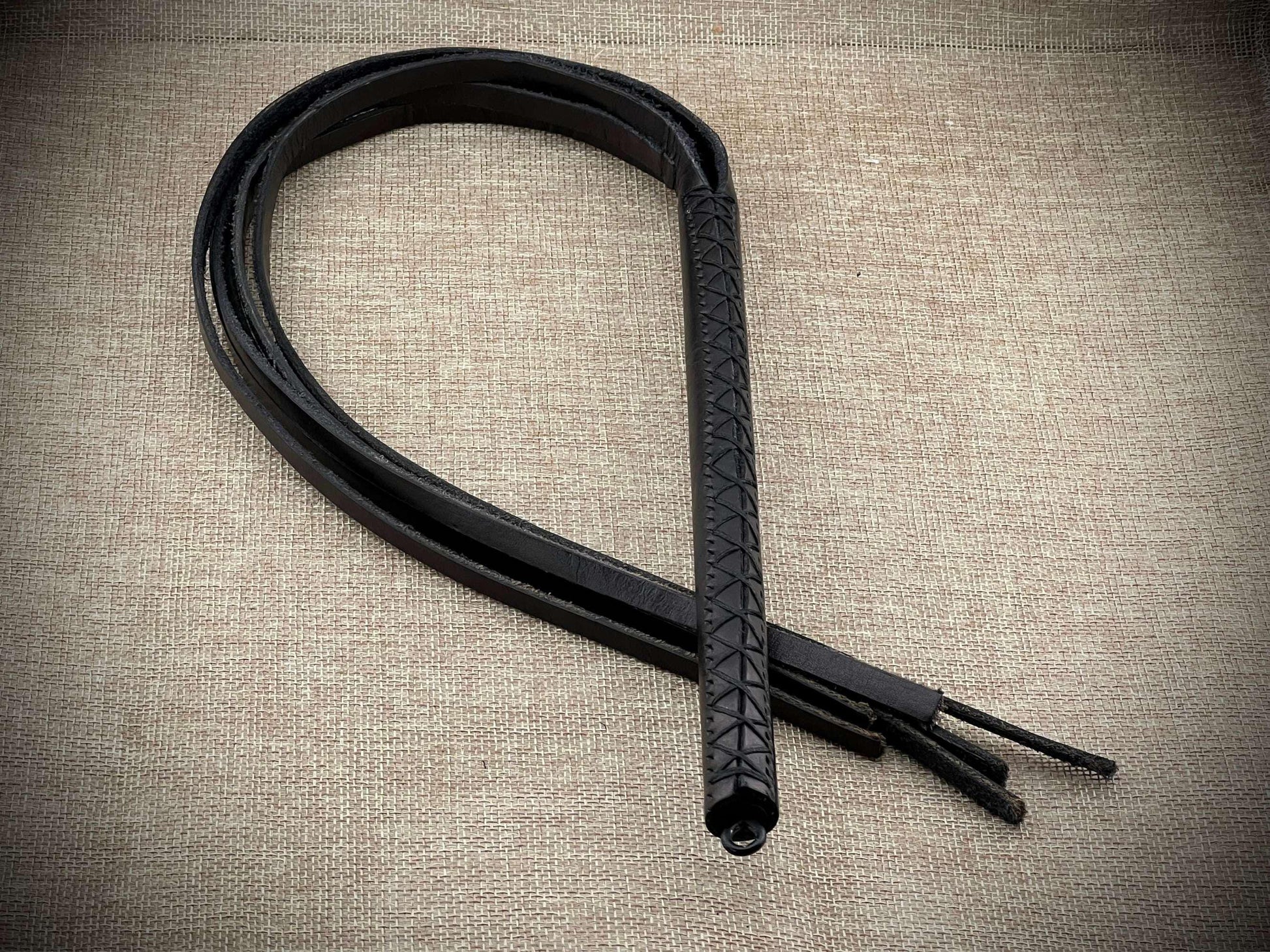 Black leather whip on a textured beige background