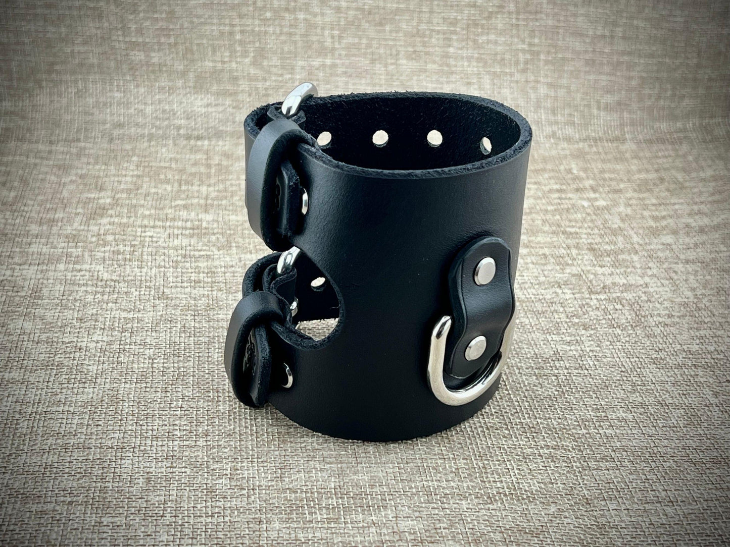Black leather wrist cuff with metal buckles on a textured gray background
