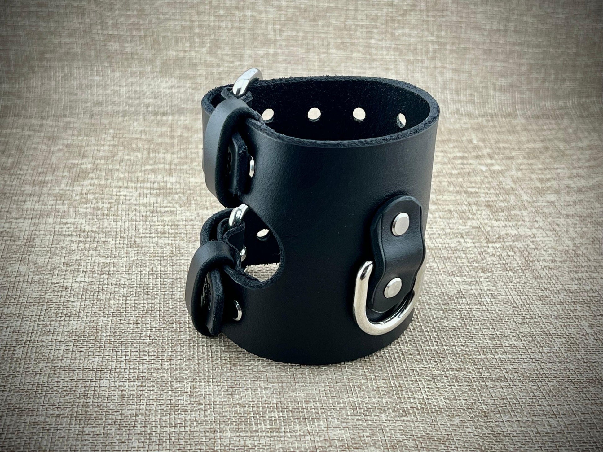 Black leather wrist cuff with metal buckles on a textured gray background