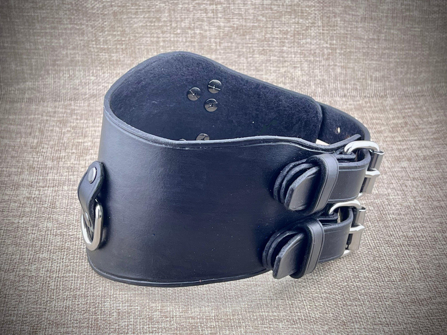 Black leather collar with metal clasps on a textured gray background