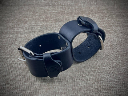 Pair of black leather cuffs on a textured gray surface