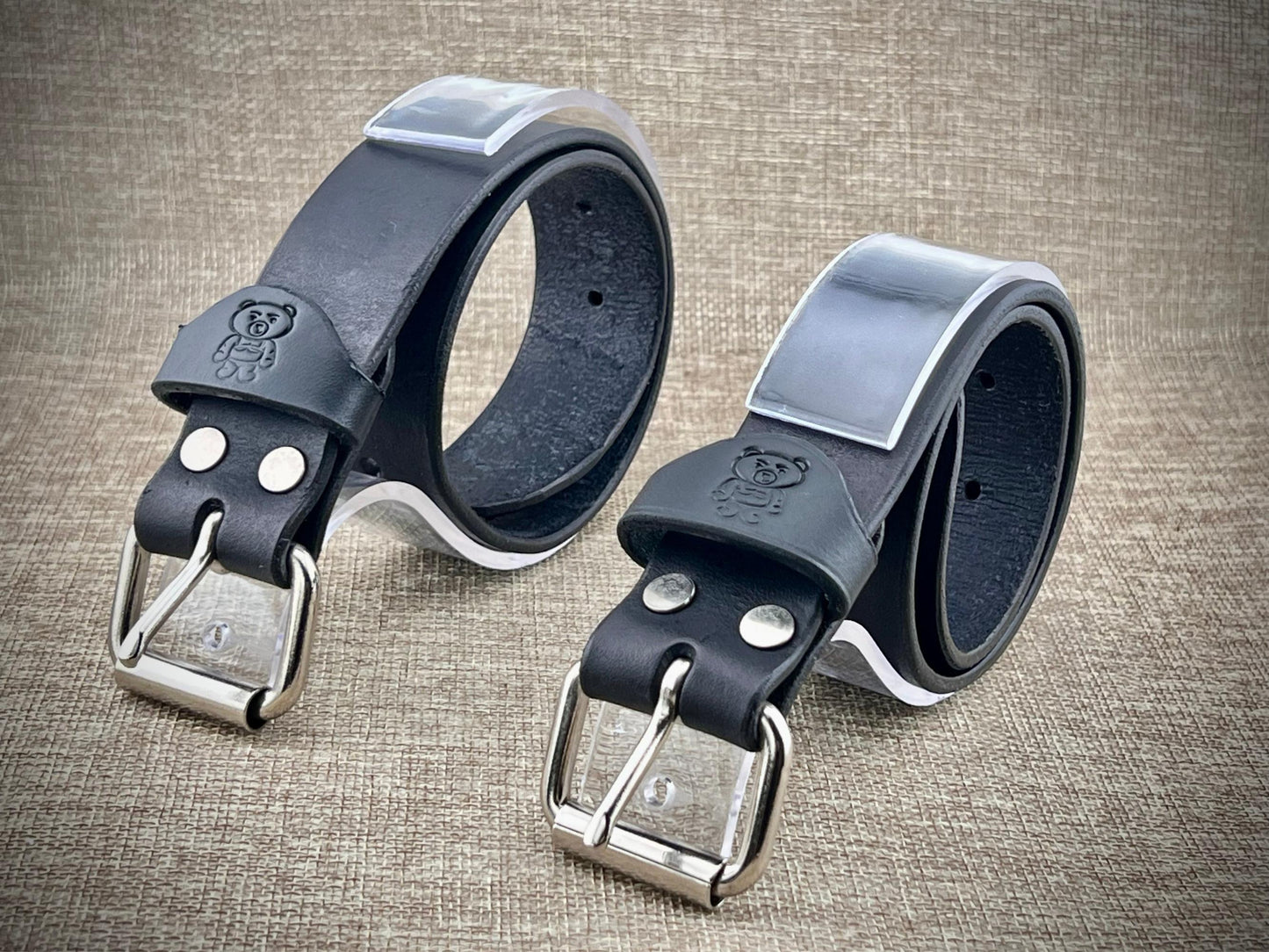 Two black leather belts with silver buckles on a textured brown background