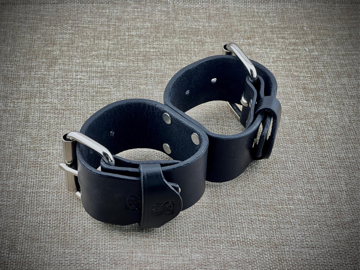 Pair of black leather cuffs on a textured gray surface