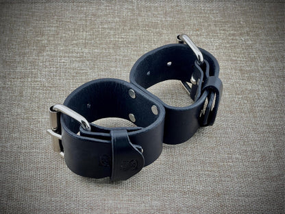 Pair of black leather cuffs on a textured gray surface