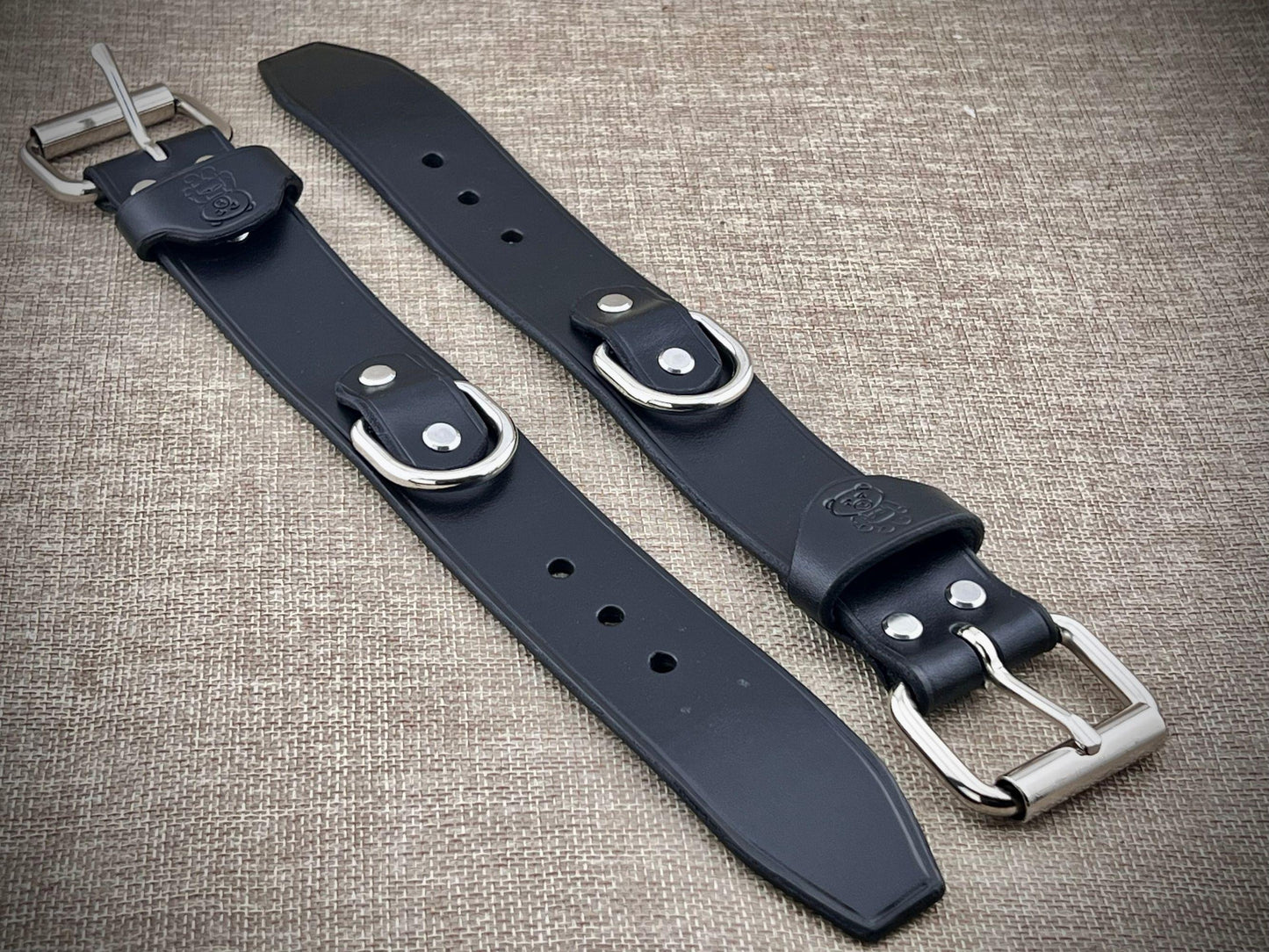 Two black leather cuffs with silver buckles on a textured surface