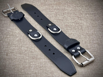 Two black leather cuffs with silver buckles on a textured surface