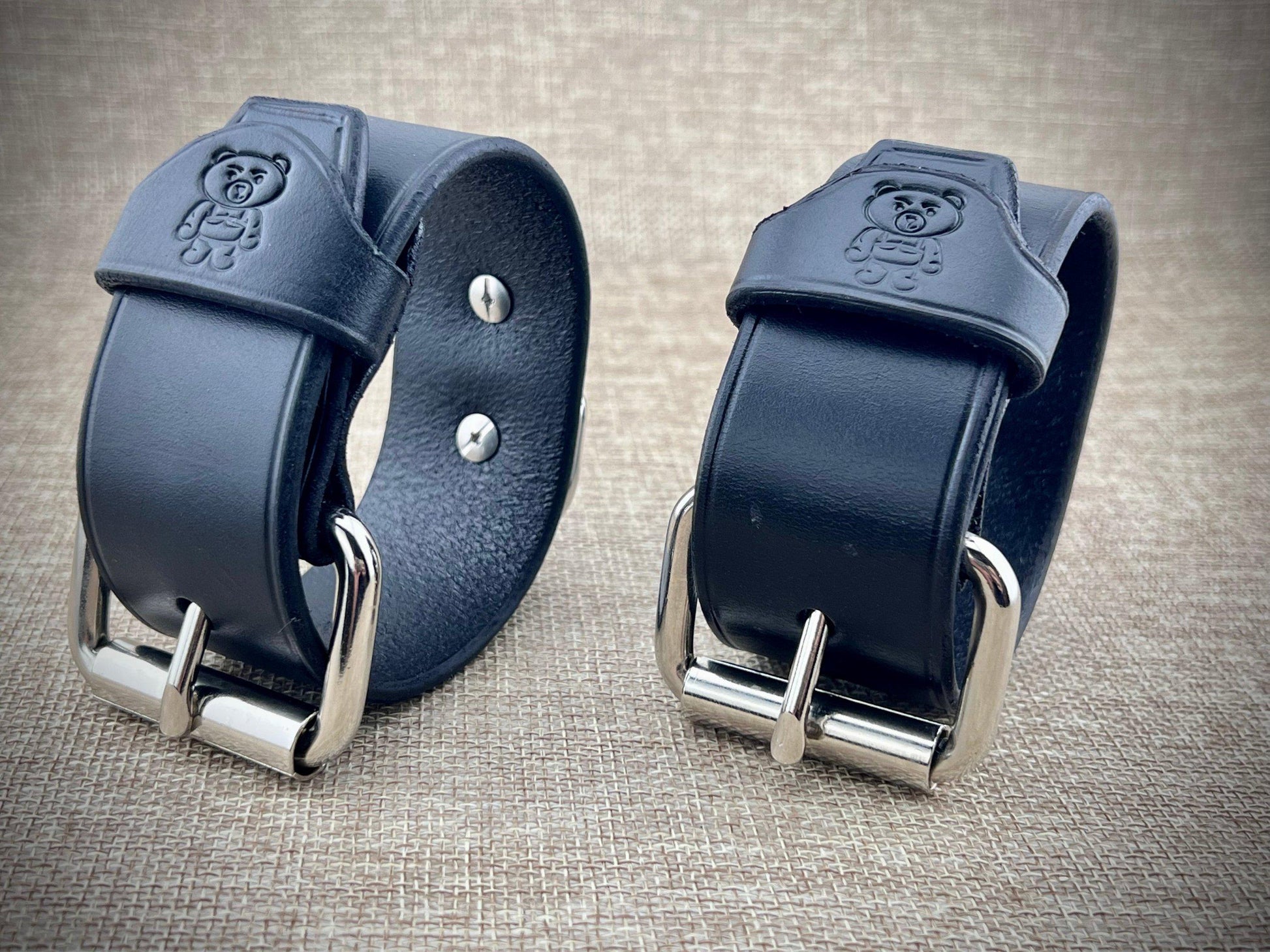 Two black leather straps with metal buckles on a textured surface