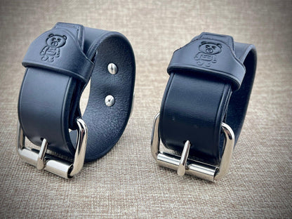 Two black leather straps with metal buckles on a textured surface