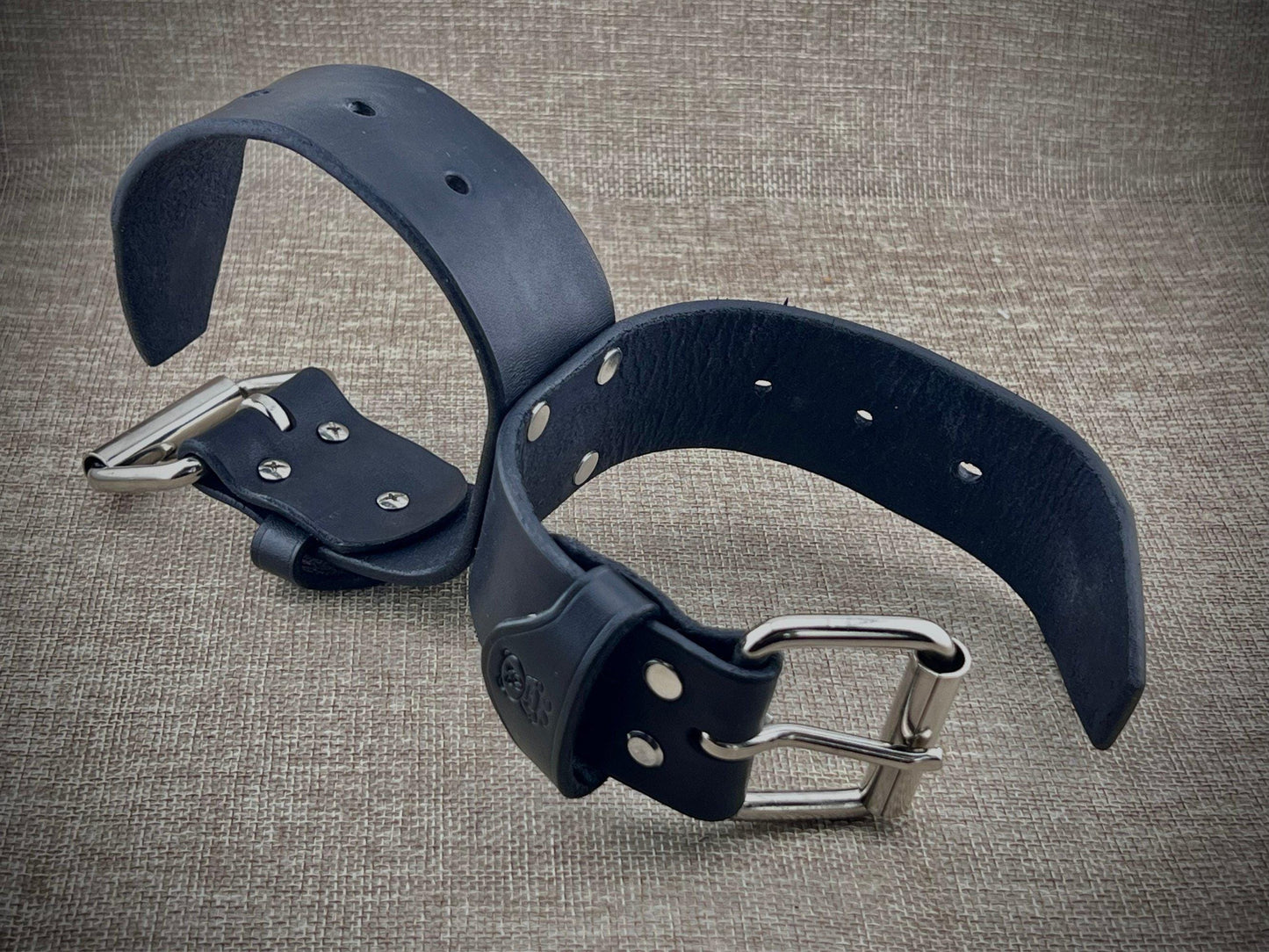 Two black connected leather wristbands with metal buckles on a textured gray background