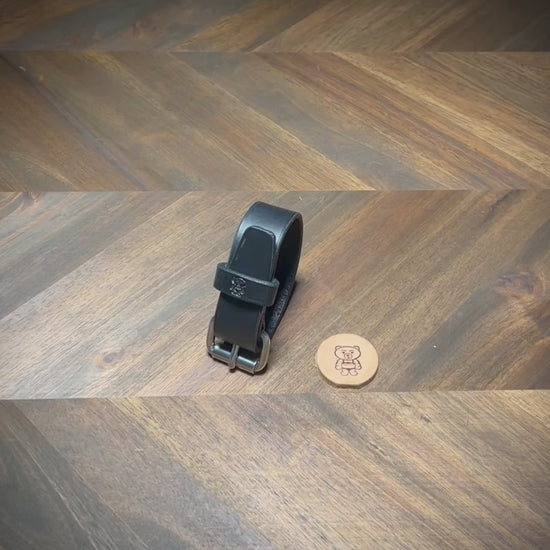 Hand-manipulating a black leather wrist cuff to demonstrate strap flexibility and steel roller buckle unfastening tracking.