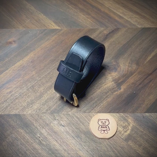 Manual demonstration unbuckling a connected black leather strap with a personalized stamped keeper and solid brass hardware.