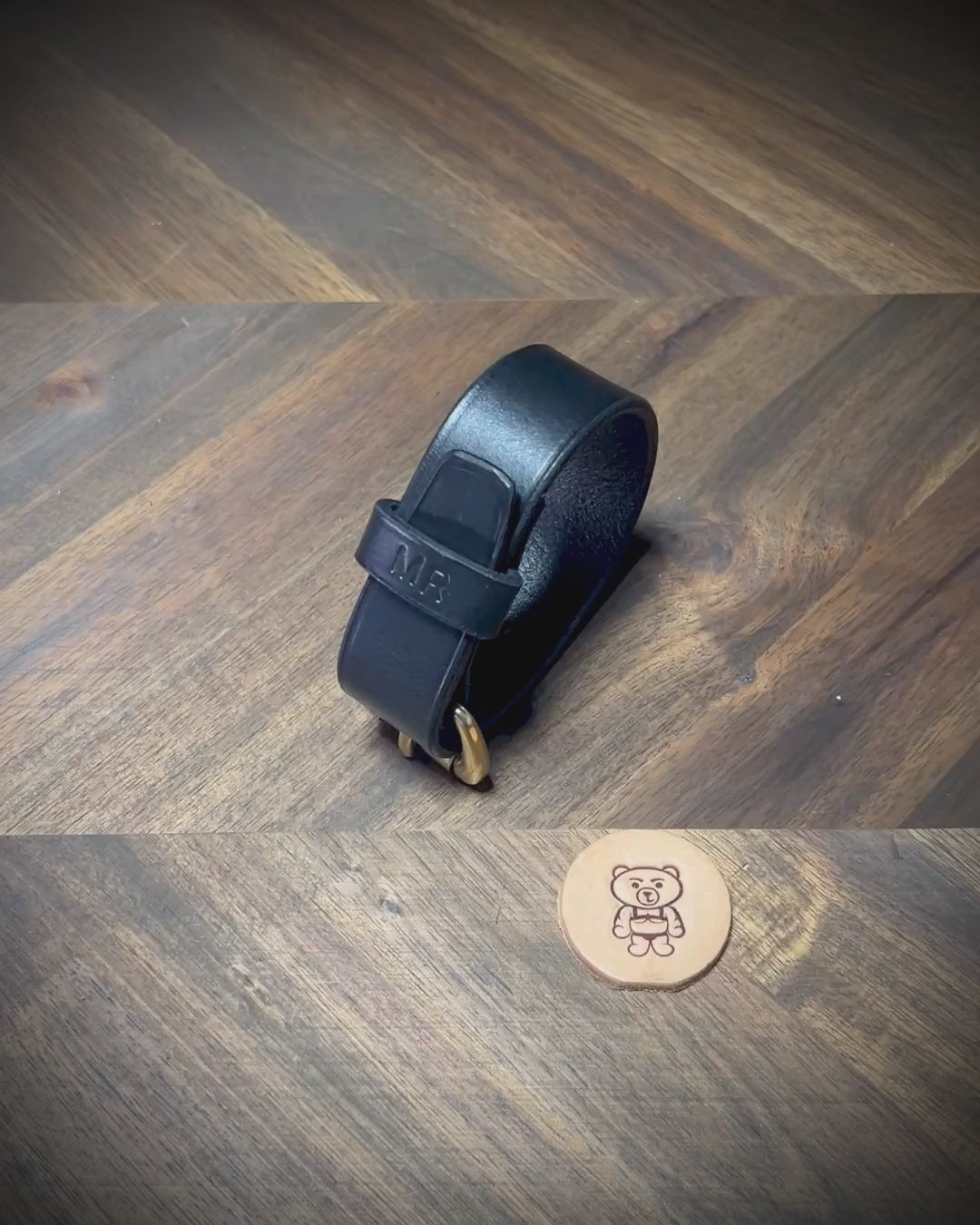 Manual demonstration unbuckling a connected black leather strap with a personalized stamped keeper and solid brass hardware.