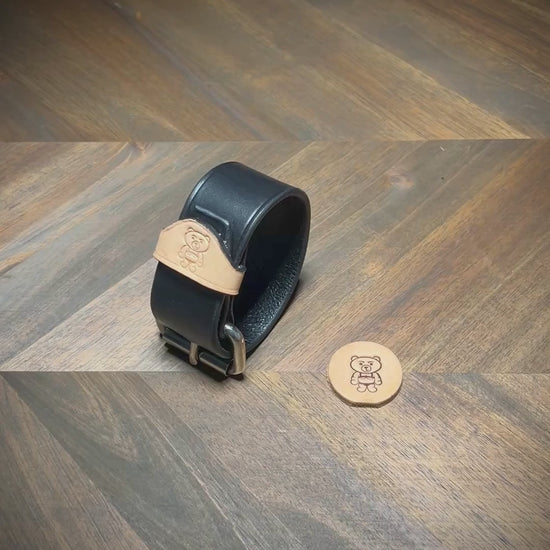 Unbuckling a 1.5" two-color leather wrist cuff to demonstrate the structural thickness of the black strap and natural leather keeper.