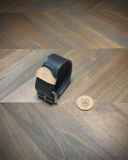 Unbuckling a 1.5" two-color leather wrist cuff to demonstrate the structural thickness of the black strap and natural leather keeper.