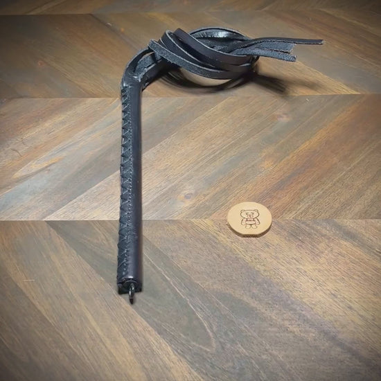 Video showing the dynamic movement and hand-burnished edges of a black leather multi-tail impact crop during a structural reveal sequence.