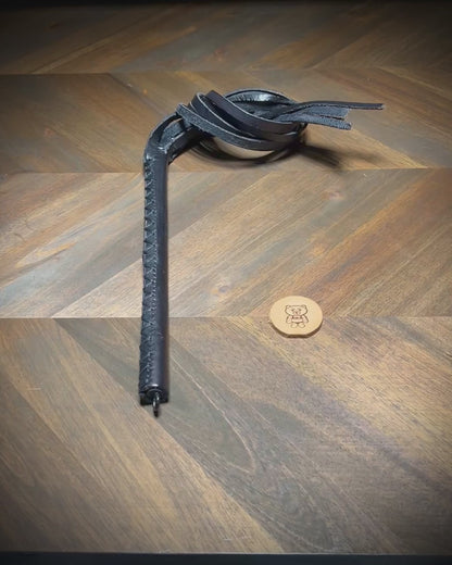 Video showing the dynamic movement and hand-burnished edges of a black leather multi-tail impact crop during a structural reveal sequence.