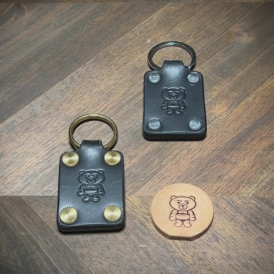 Hand-testing the structural integrity and displaying the hardware variations of two black leather keychains.