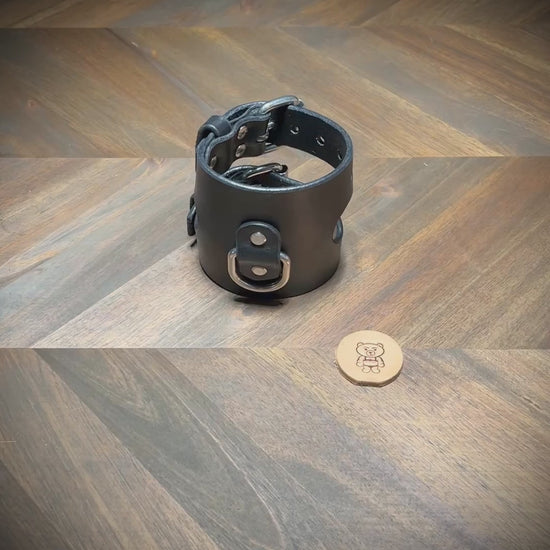Demonstrating the dual unbuckling action and laying flat of a 3.5" wide black leather restraint cuff with nickel-plated steel hardware.