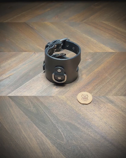 Demonstrating the dual unbuckling action and laying flat of a 3.5" wide black leather restraint cuff with nickel-plated steel hardware.