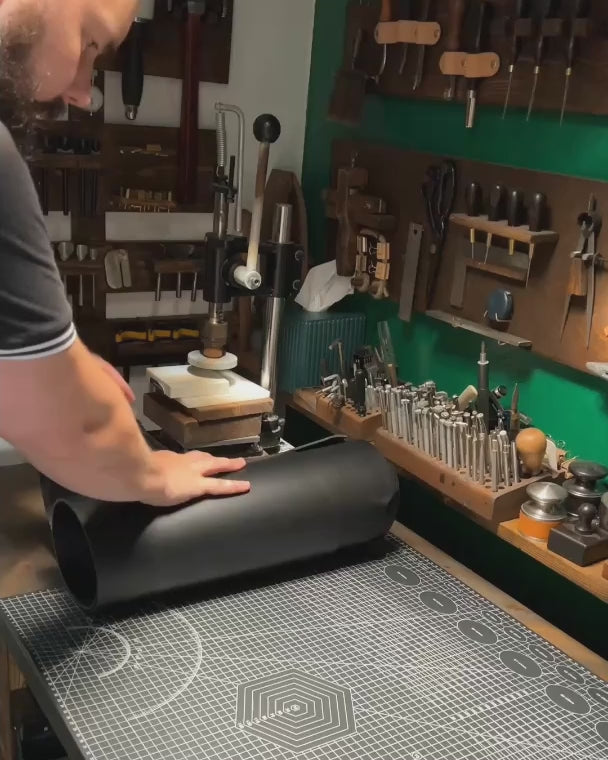 Bearded artisan at Knotty Oso, Miami Beach, hand-crafting premium black veg-tanned leather accessory with hand tools at a workshop bench.