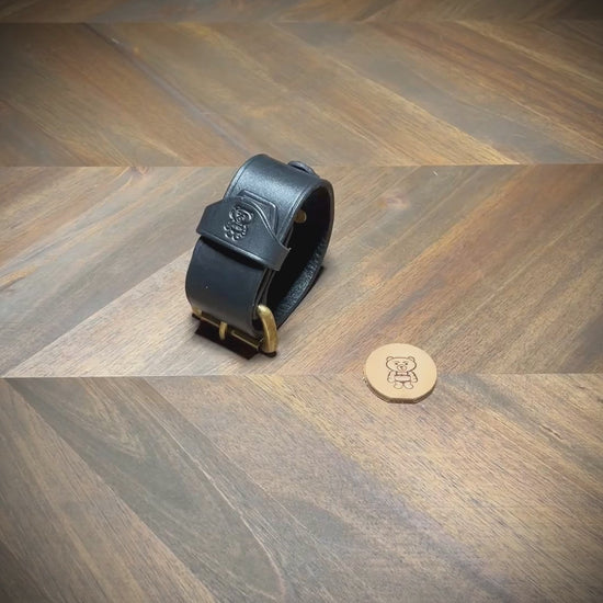 Demonstrating the unbuckling, structural flexibility, interior grain texture, and hardware alignment of a 1.5" black leather cuff with an integrated D-ring.