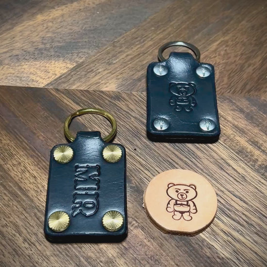 Hands inspecting custom initialed black leather keychains with steel and brass hardware.