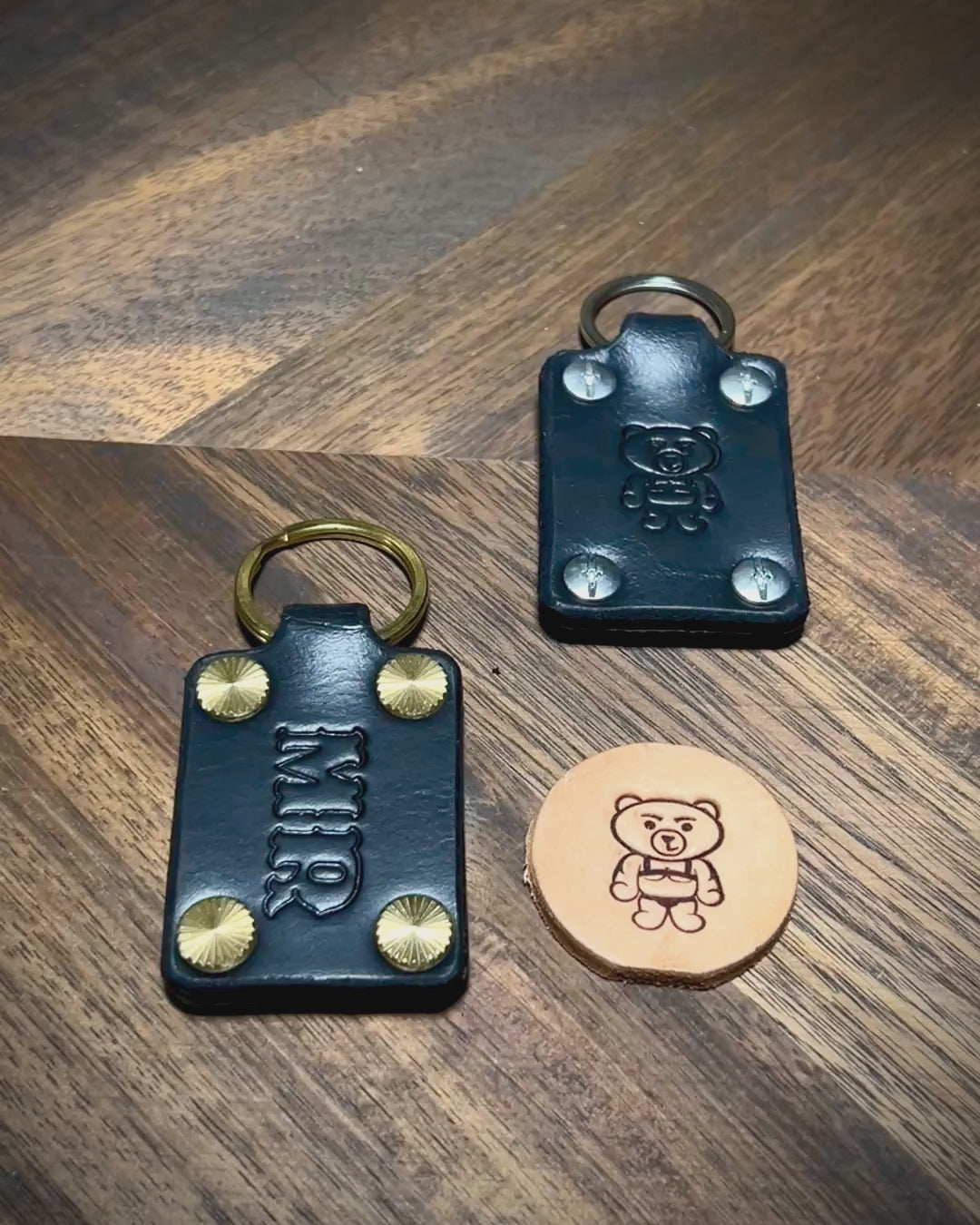 Hands inspecting custom initialed black leather keychains with steel and brass hardware.