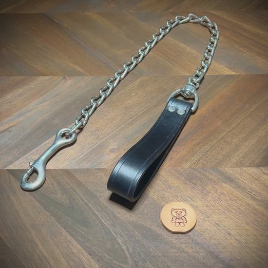 Hand-demonstrating the structural flexibility, rivet alignment, and heavy-duty snap mechanism of a black leather loop tether with steel chain.