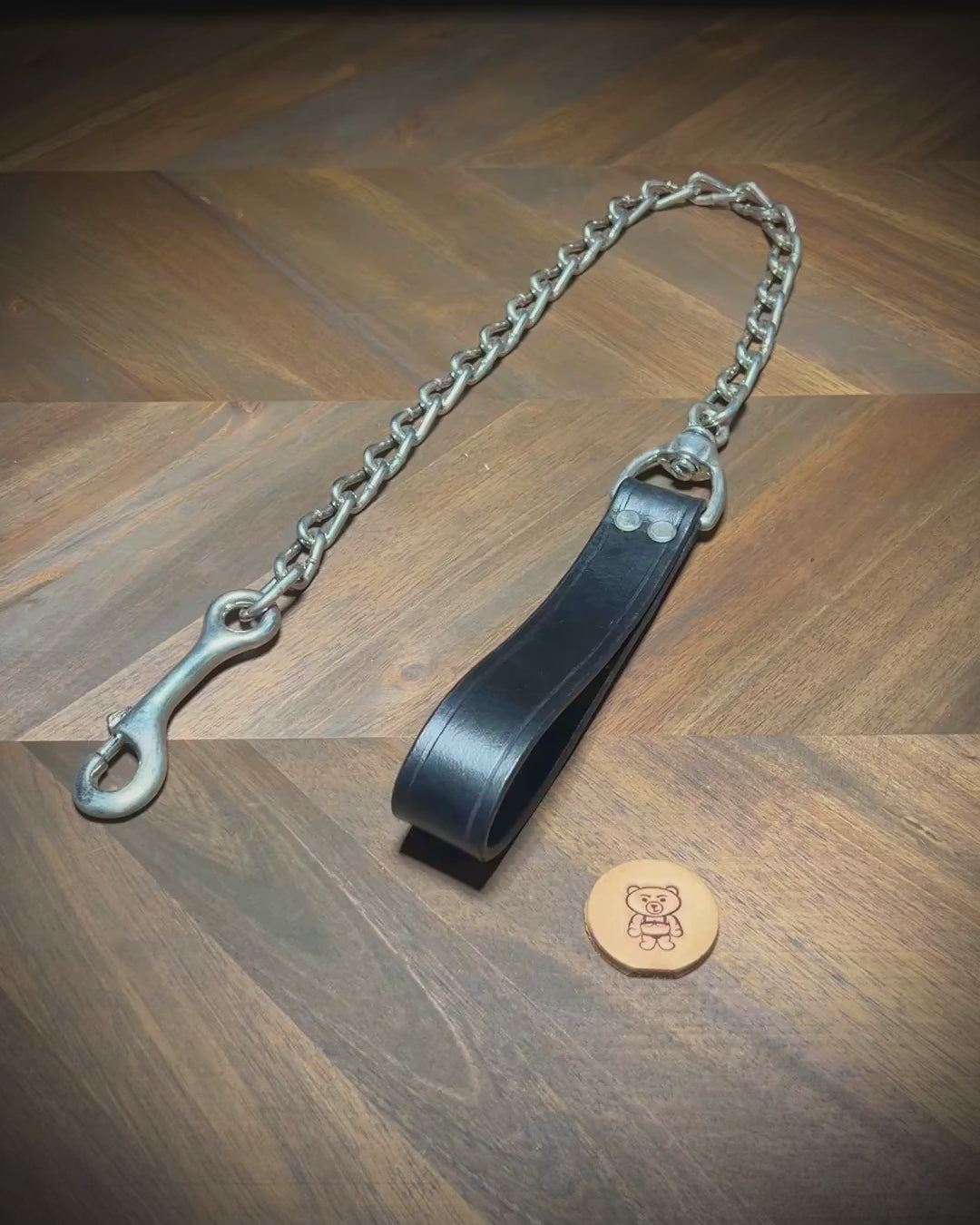Hand-demonstrating the structural flexibility, rivet alignment, and heavy-duty snap mechanism of a black leather loop tether with steel chain.