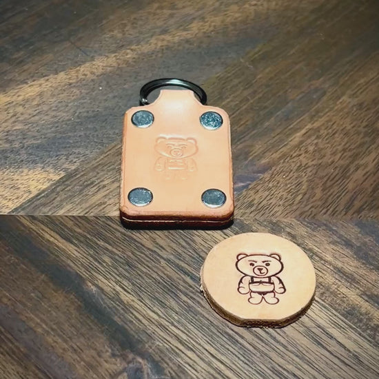 Manual demonstration inspecting edges, nickel hardware, and embossed logo on natural leather keychain.