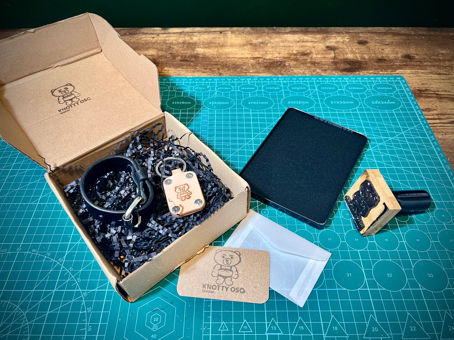 Box of leather accessories including a collar, leash, and tags on a cutting mat.