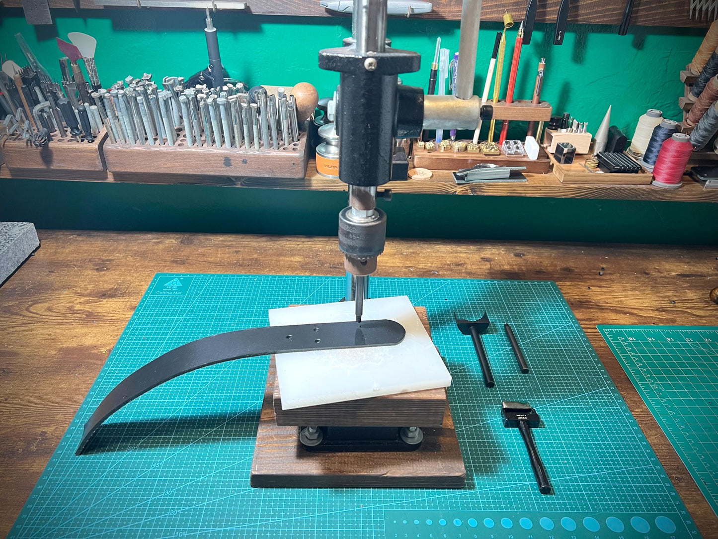 Workbench with metalworking tools and equipment, including a drill press and metal rod.