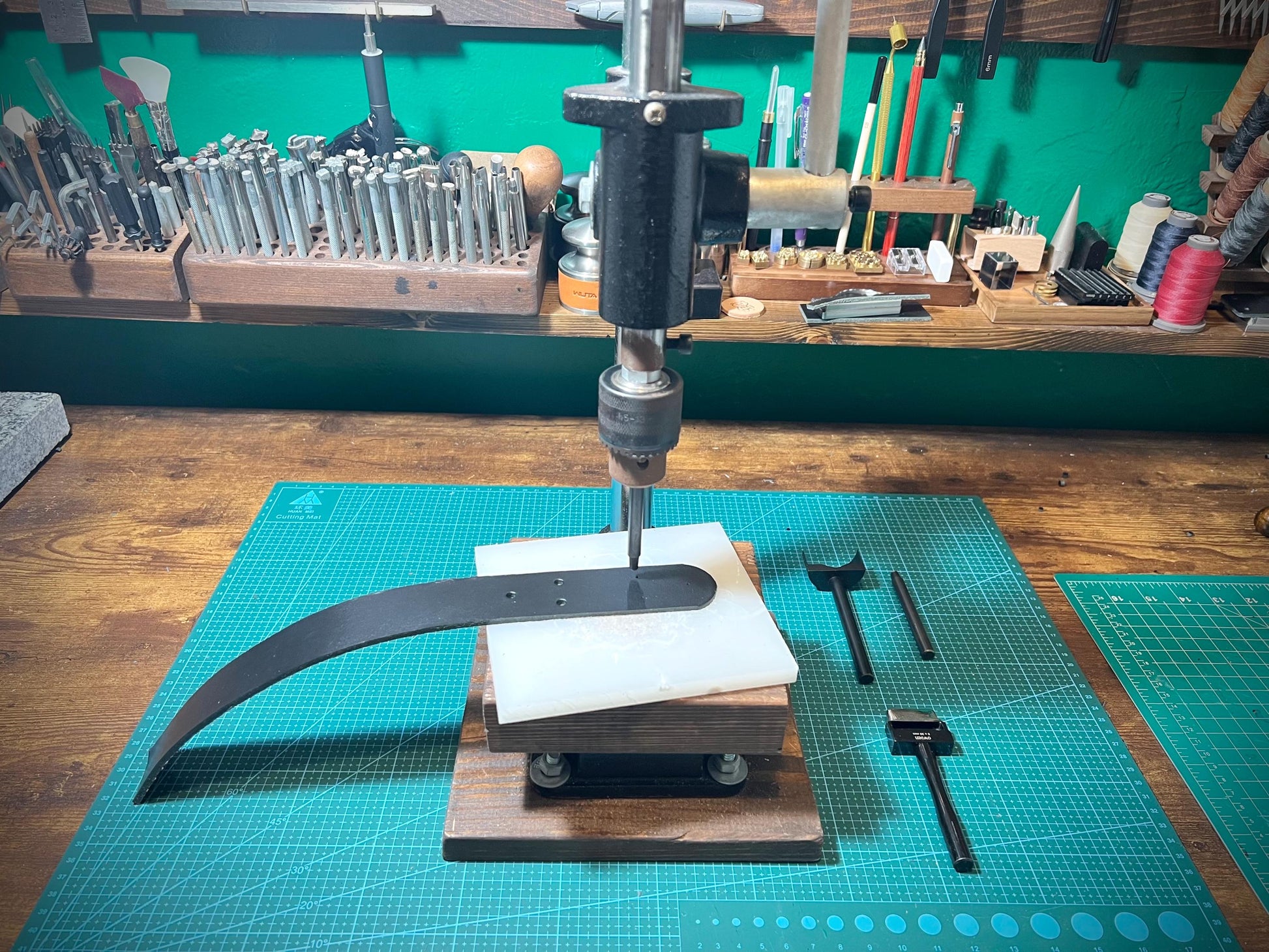 Workbench with metalworking tools and equipment, including a drill press and metal rod.
