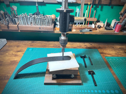 Workbench with metalworking tools and equipment, including a drill press and metal rod.