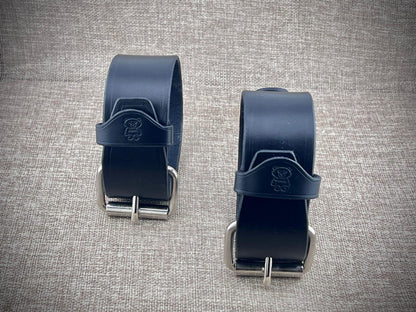 Two black leather bands with metal buckles on a textured gray background