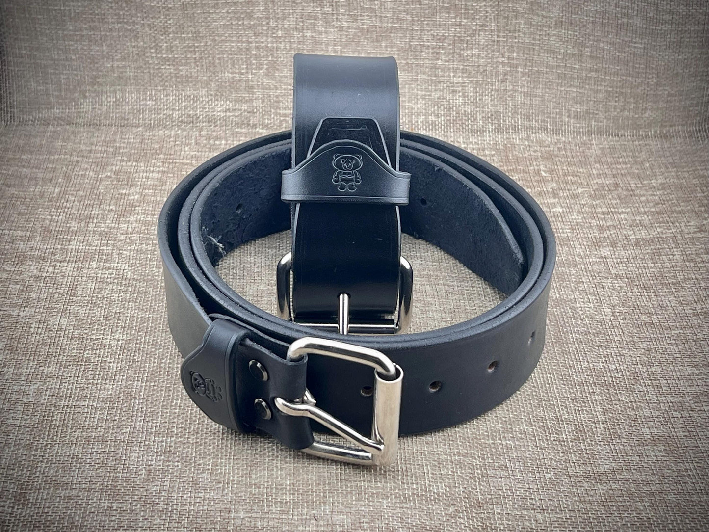 Black leather belt with silver buckle on a textured gray background