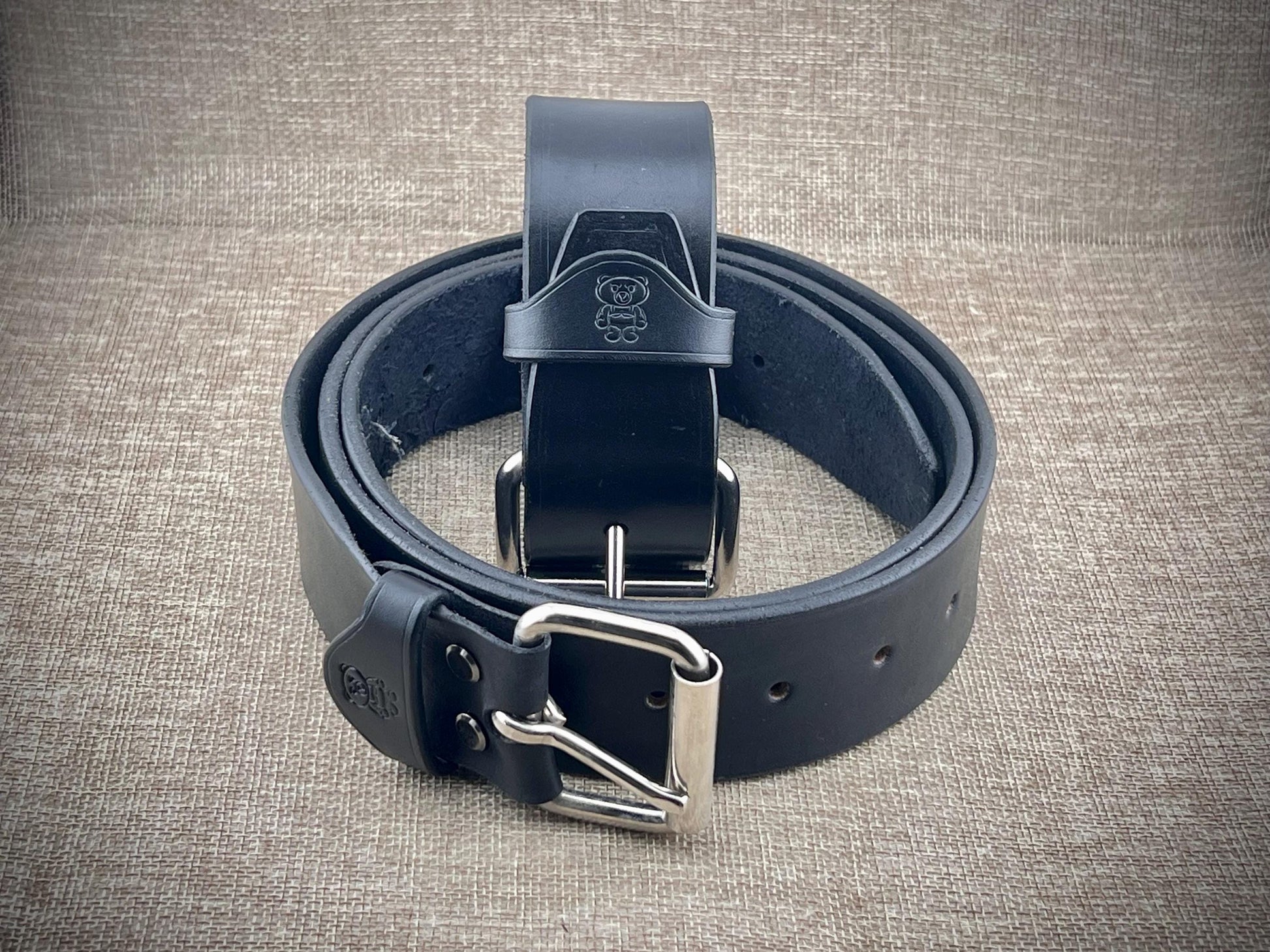 Black leather belt with silver buckle on a textured gray background