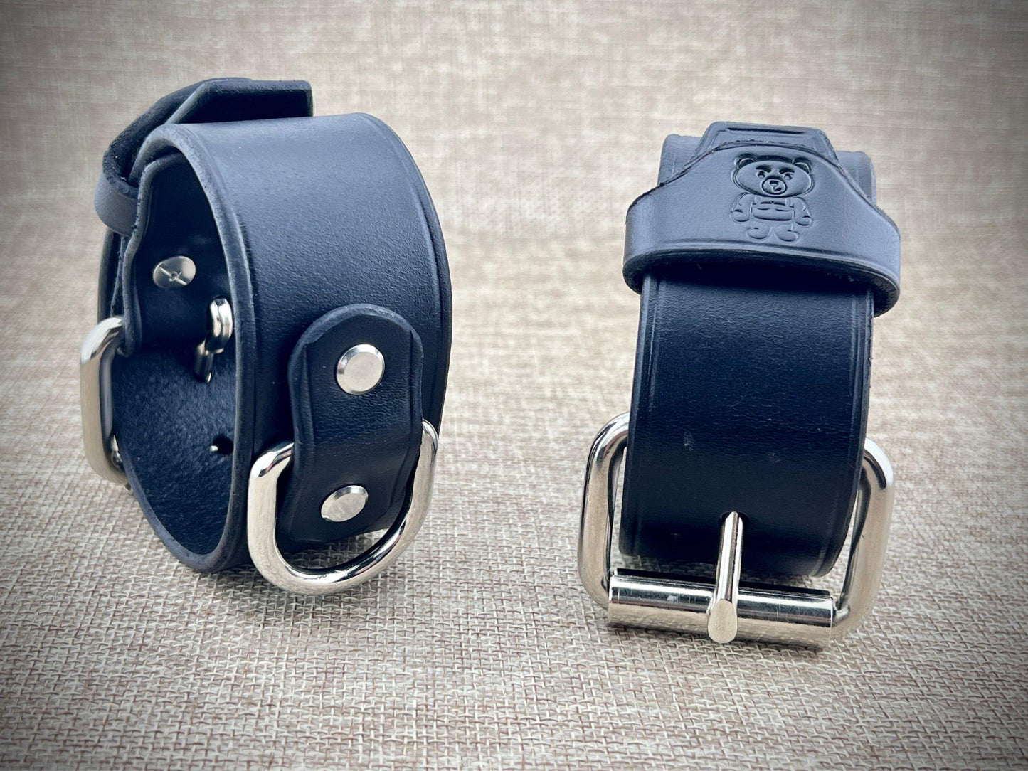 Two black leather cuffs with metal buckles on a textured gray background