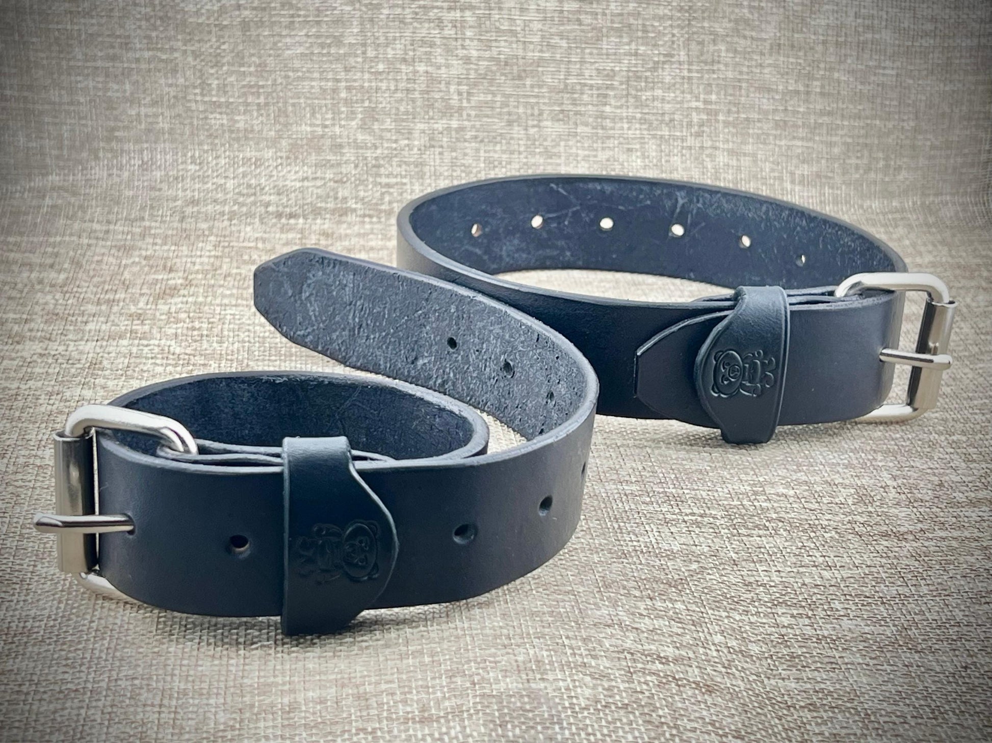 Two black leather straps with metal buckles on a textured gray background