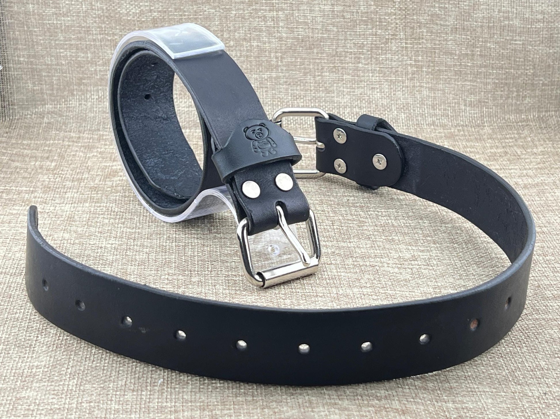Two bondage belts with silver buckle on a textured beige background