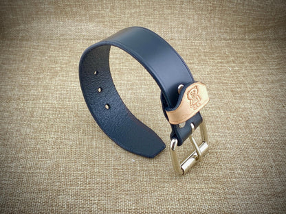 Black leather cuff with a gold buckle on a textured brown background