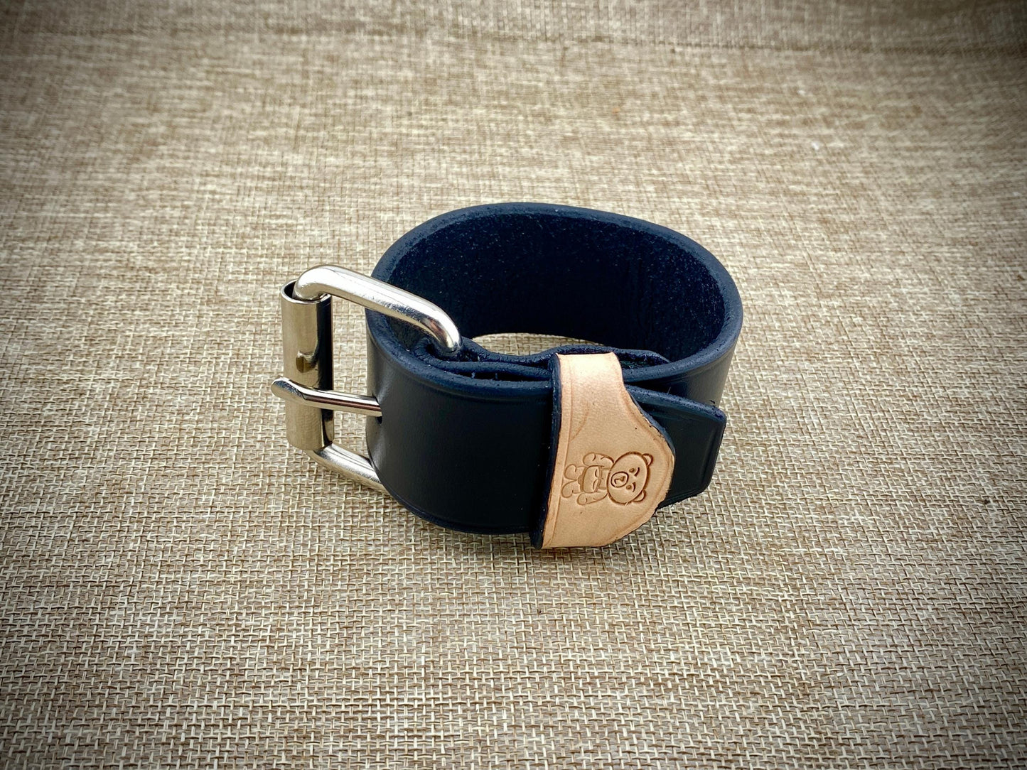 Black leather belt with steel buckle on a textured beige background