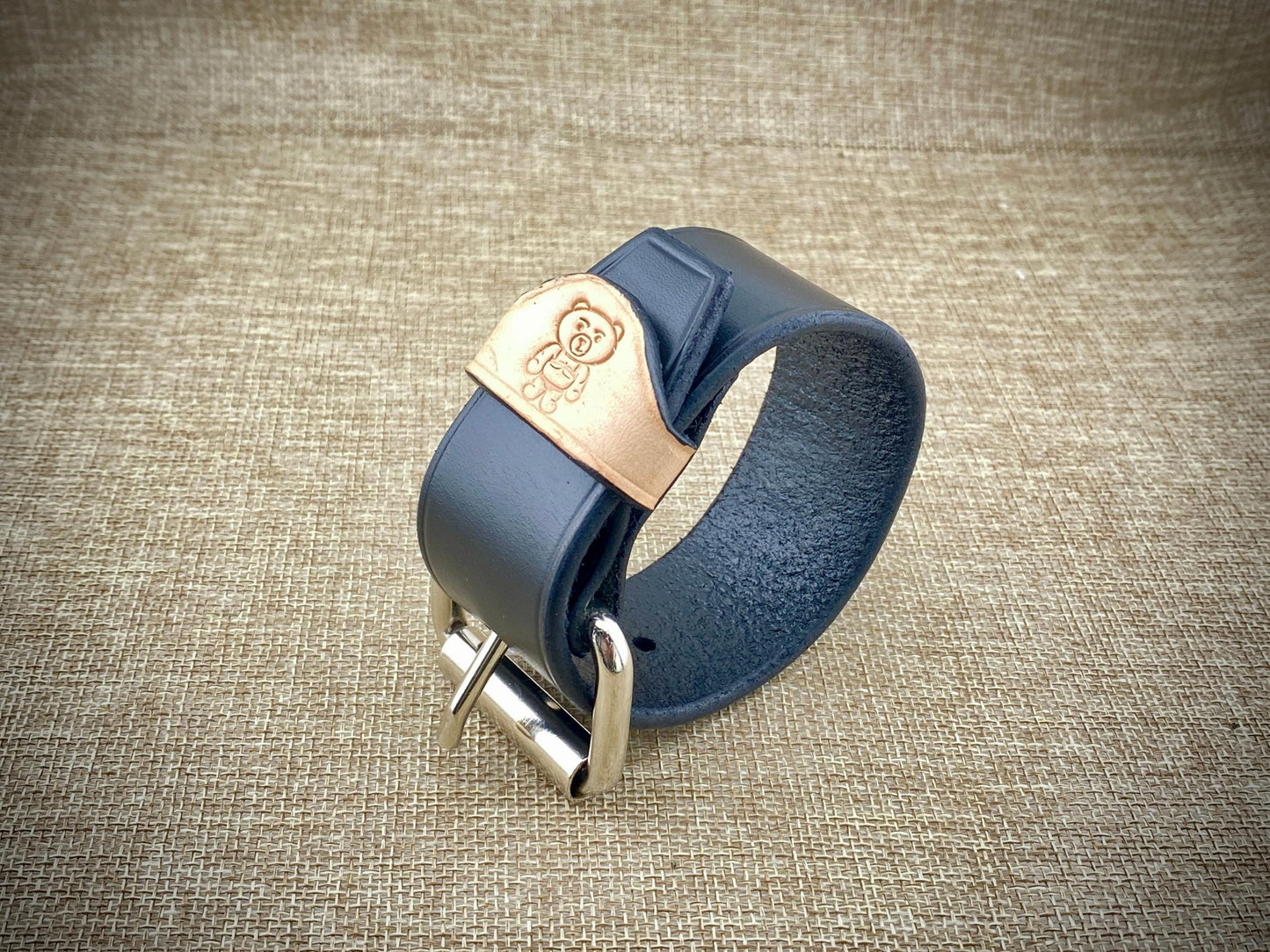 Black leather bracelet with steel buckle on a textured brown background