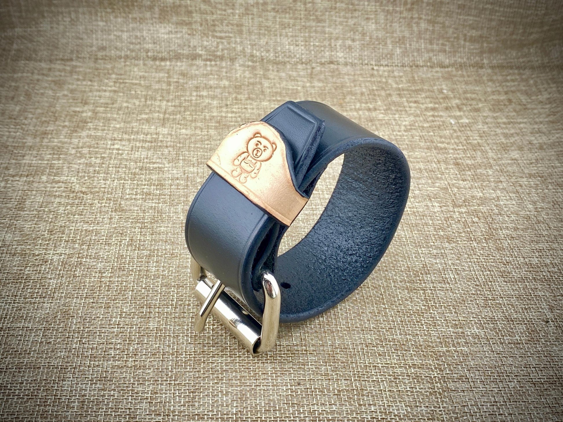 Black leather bracelet with steel buckle on a textured brown background