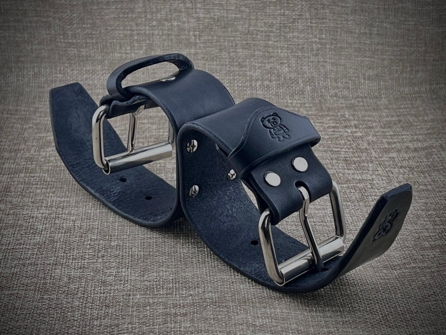 Black leather cuffs with steel buckle on a textured gray background