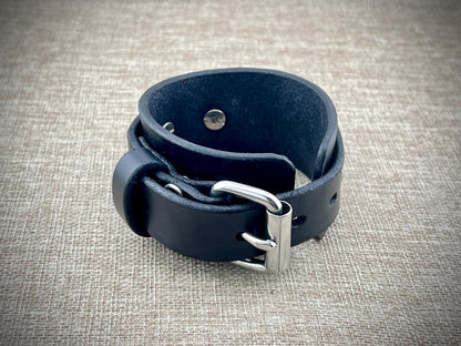Black leather bracelet with silver buckle on a textured beige background