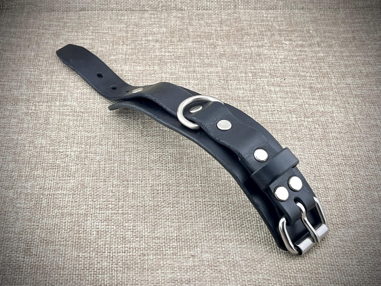 Black leather cuff with silver hardware on a textured beige background