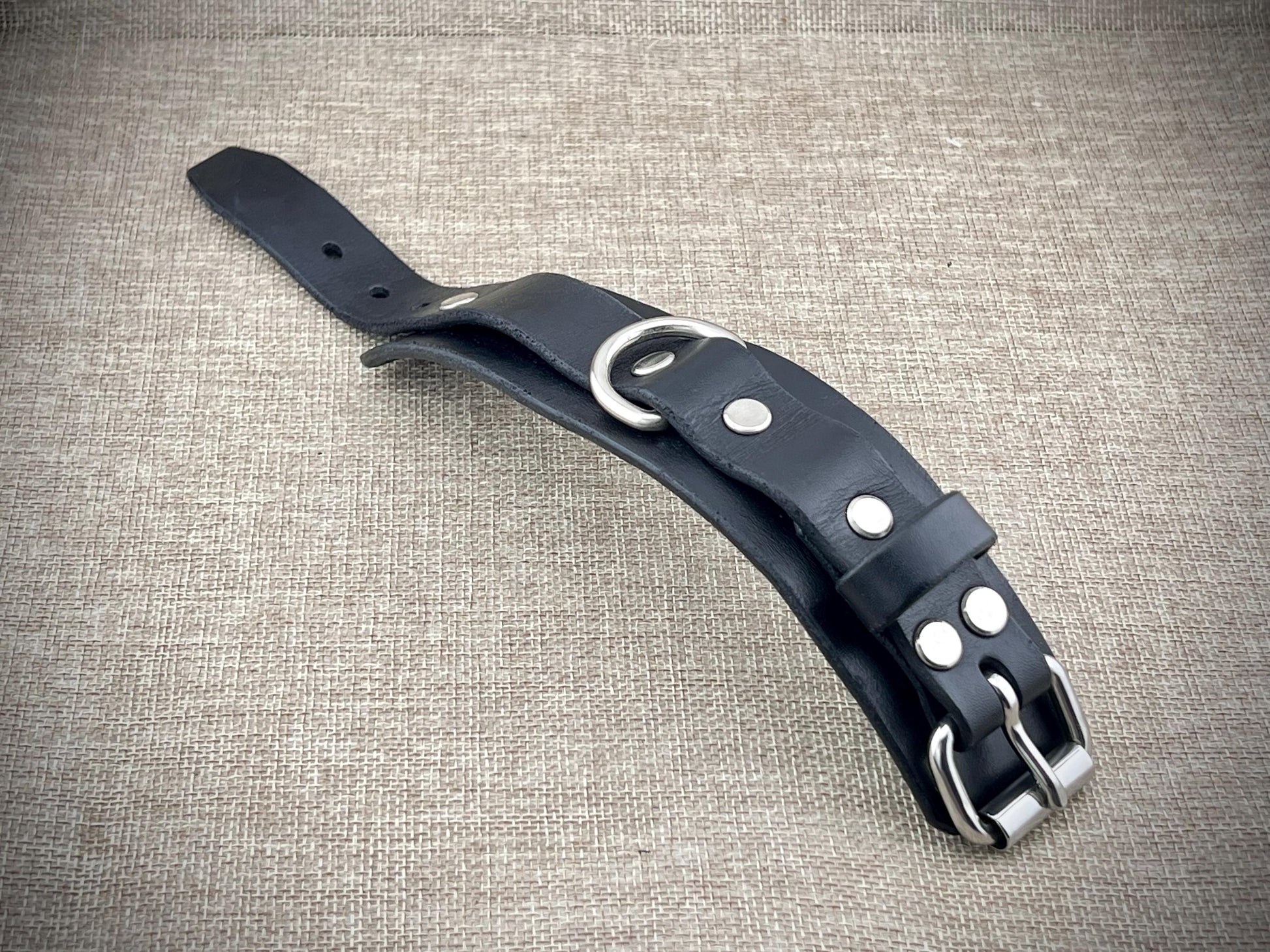 Black leather cuff with silver hardware on a textured beige background
